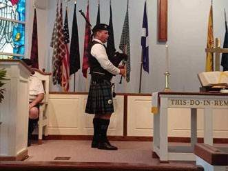 Person playing bagpipe in a church in front of flags